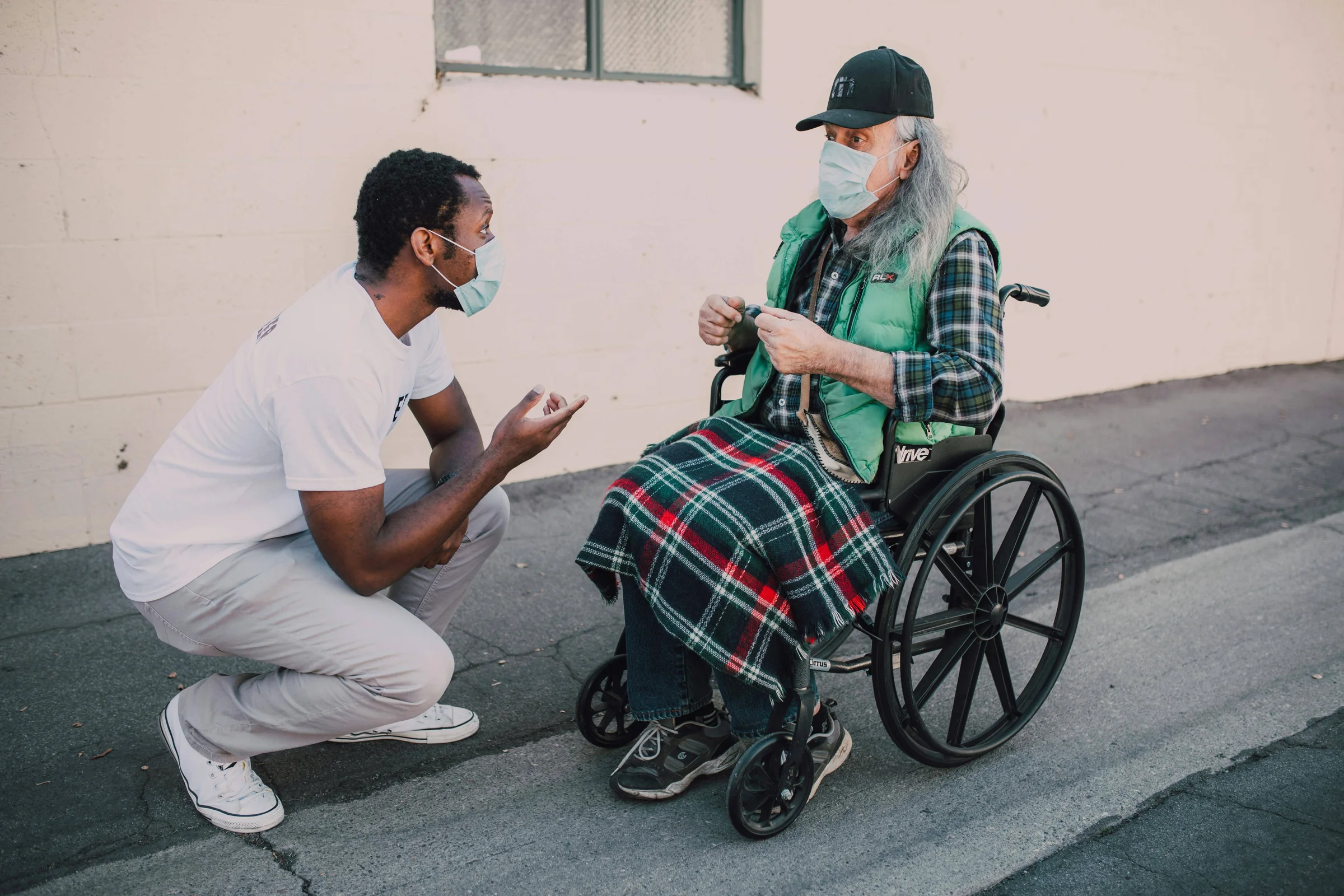 A young man kneels to talk with an elderly woman in a wheelchair