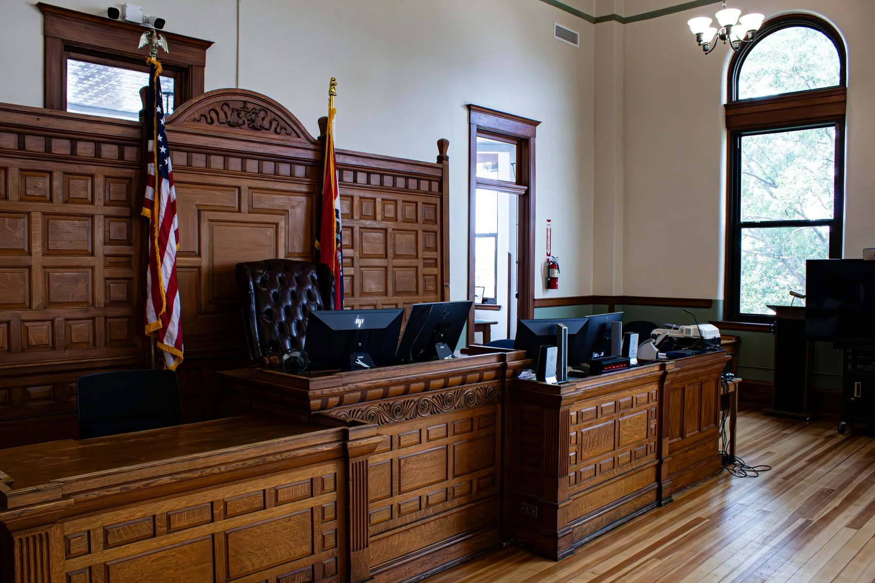 An empty courtroom with a judge’s bench and flags