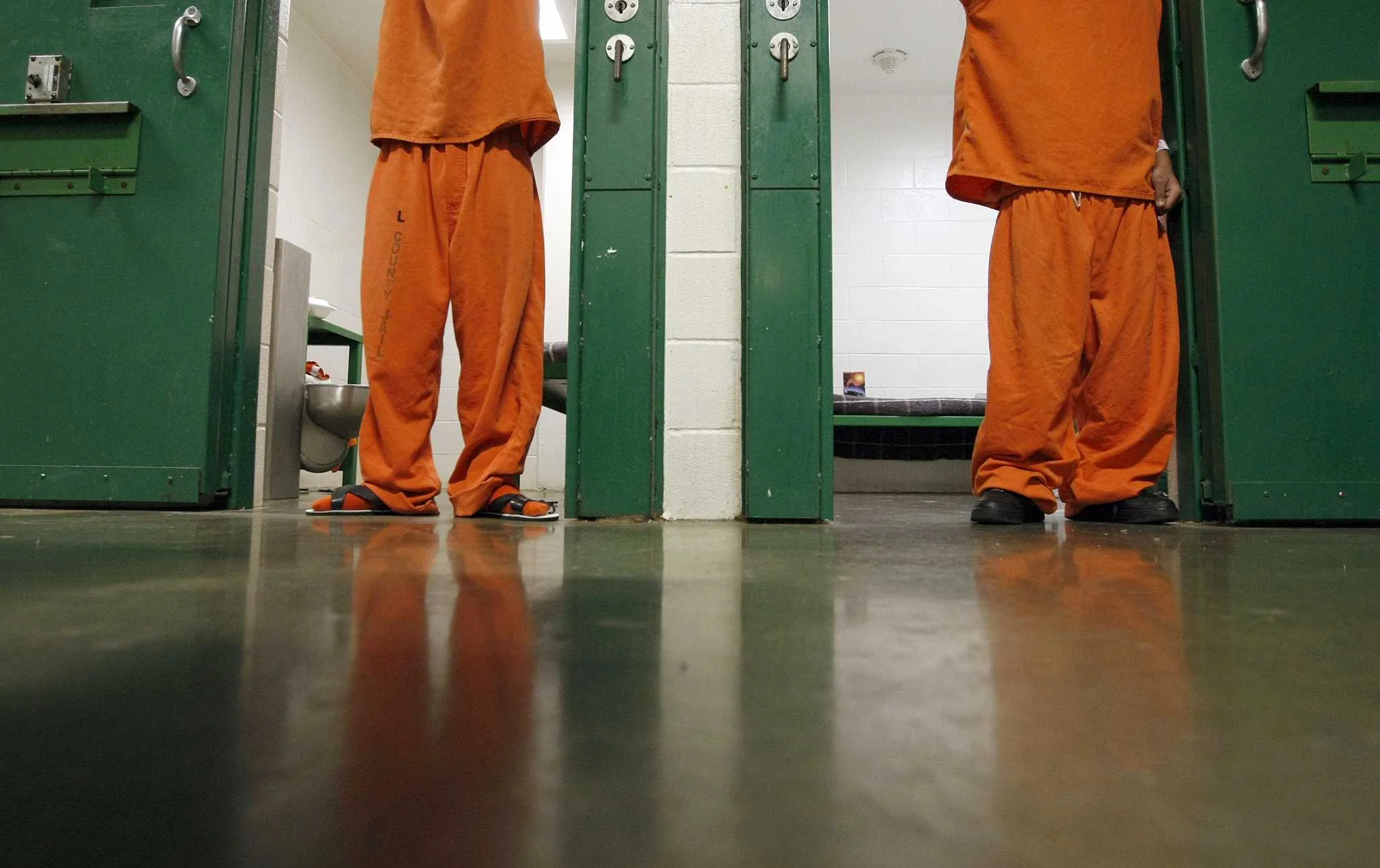 Two young people in orange detention uniforms stand at the doors of their cells