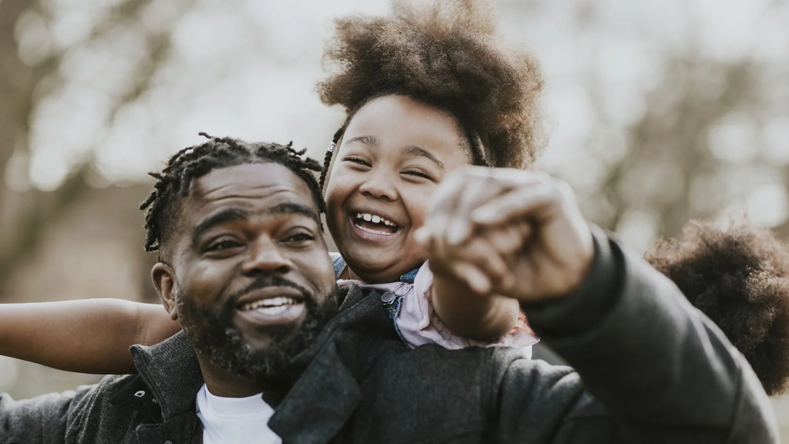 A father laughs with his son on his shoulders