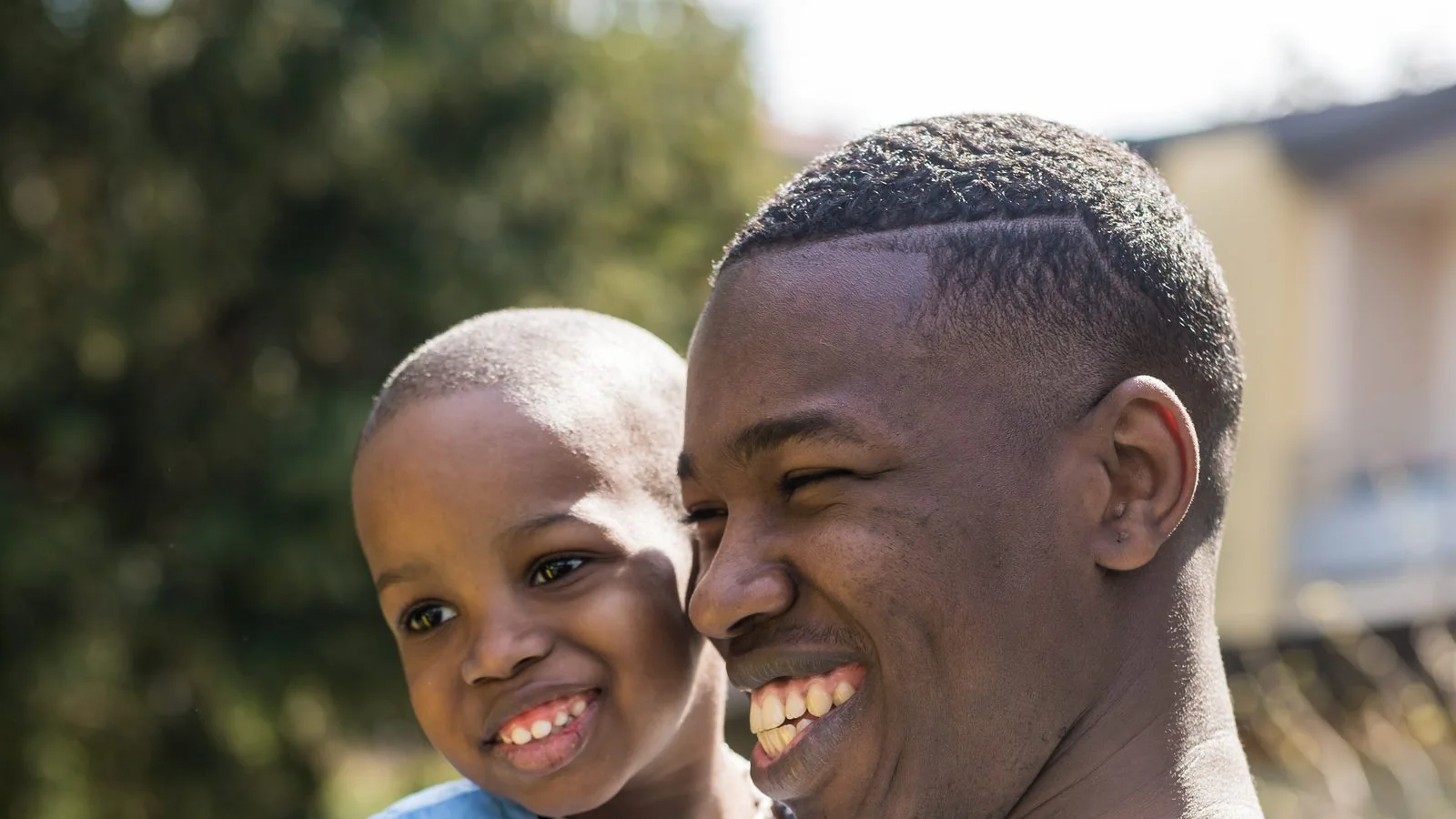 A young father smiles with his son outdoors