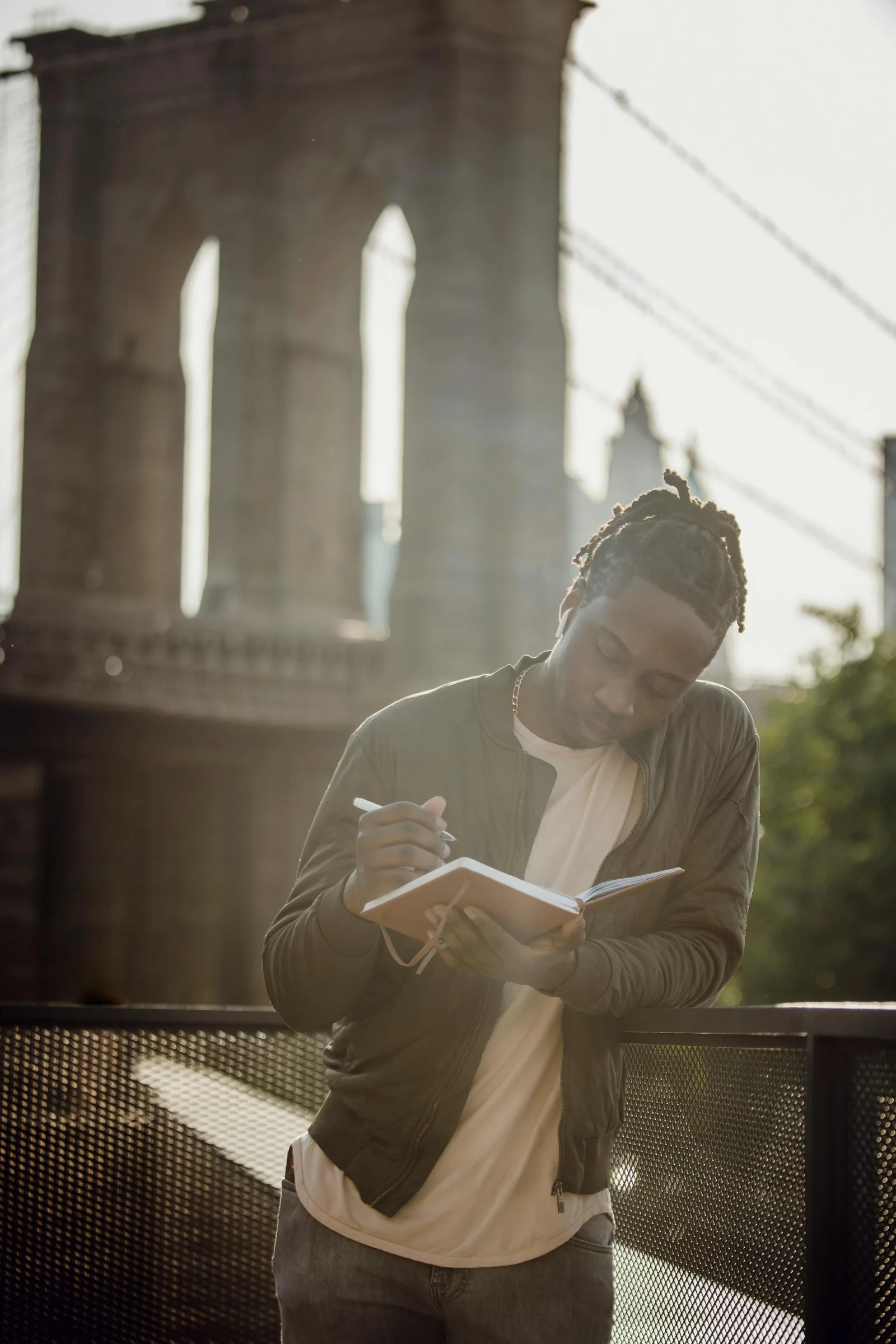A man writing in a notebook under a city bridge