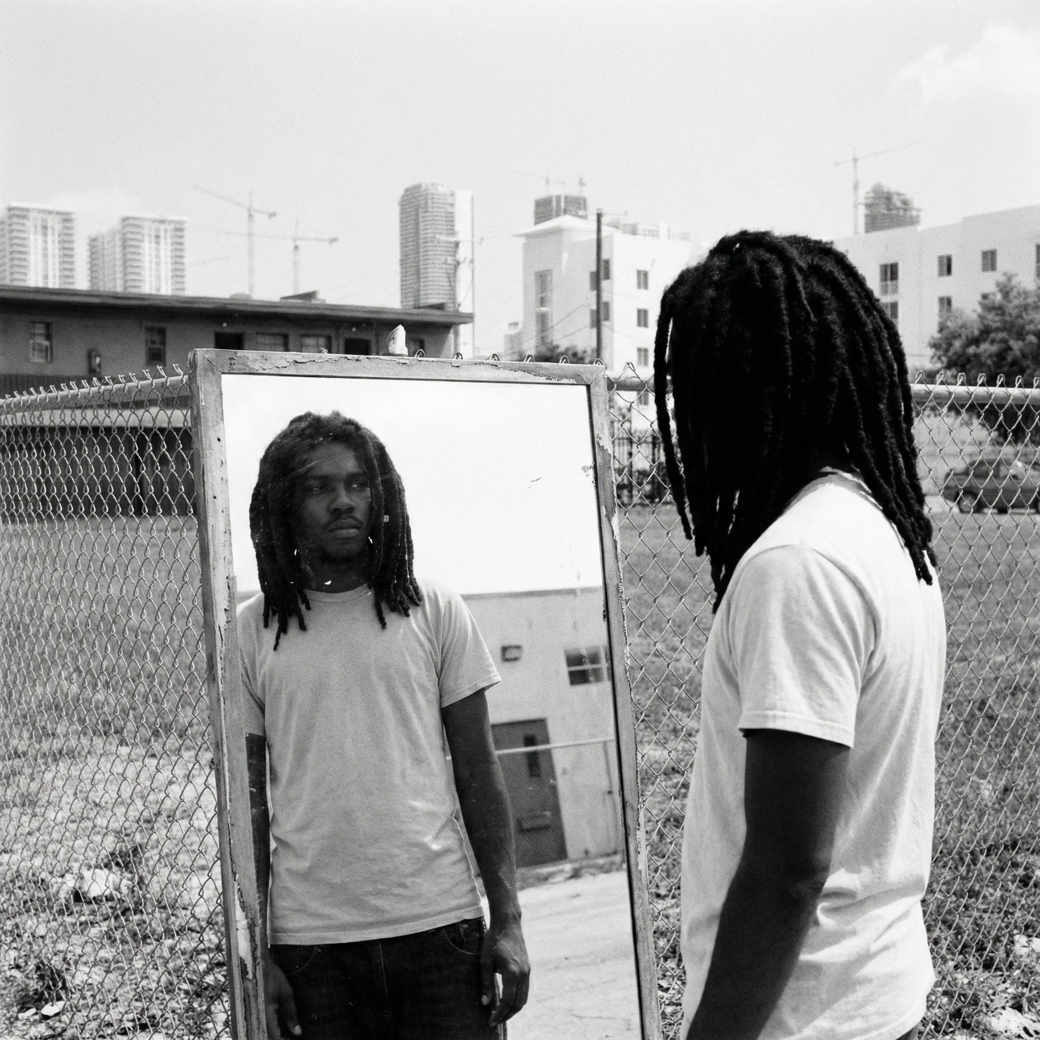 A young man looks at himself in a weathered mirror leaning on a fence in Miami