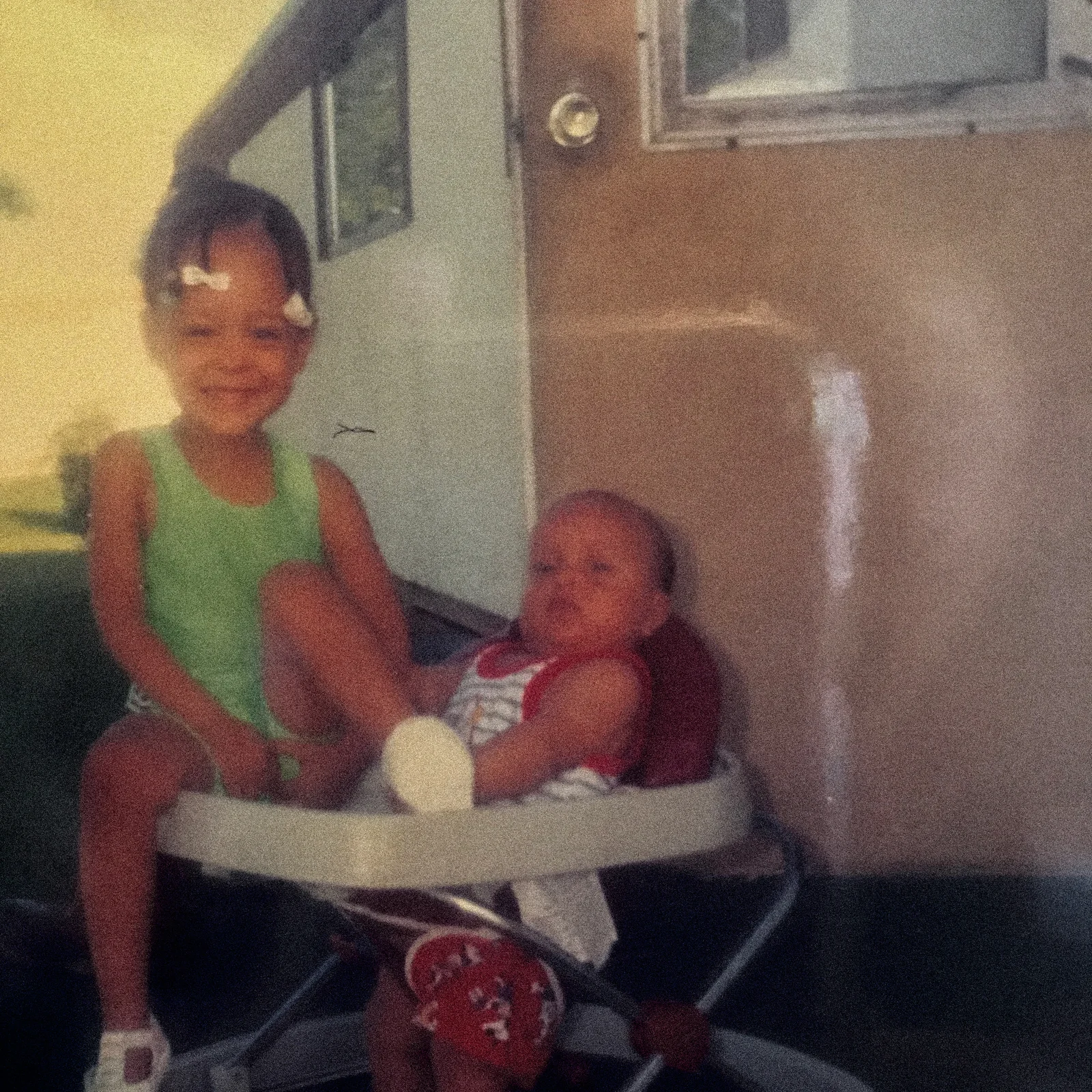 Ronnie Lillard as a baby in a walker beside his older sister, outside a trailer home