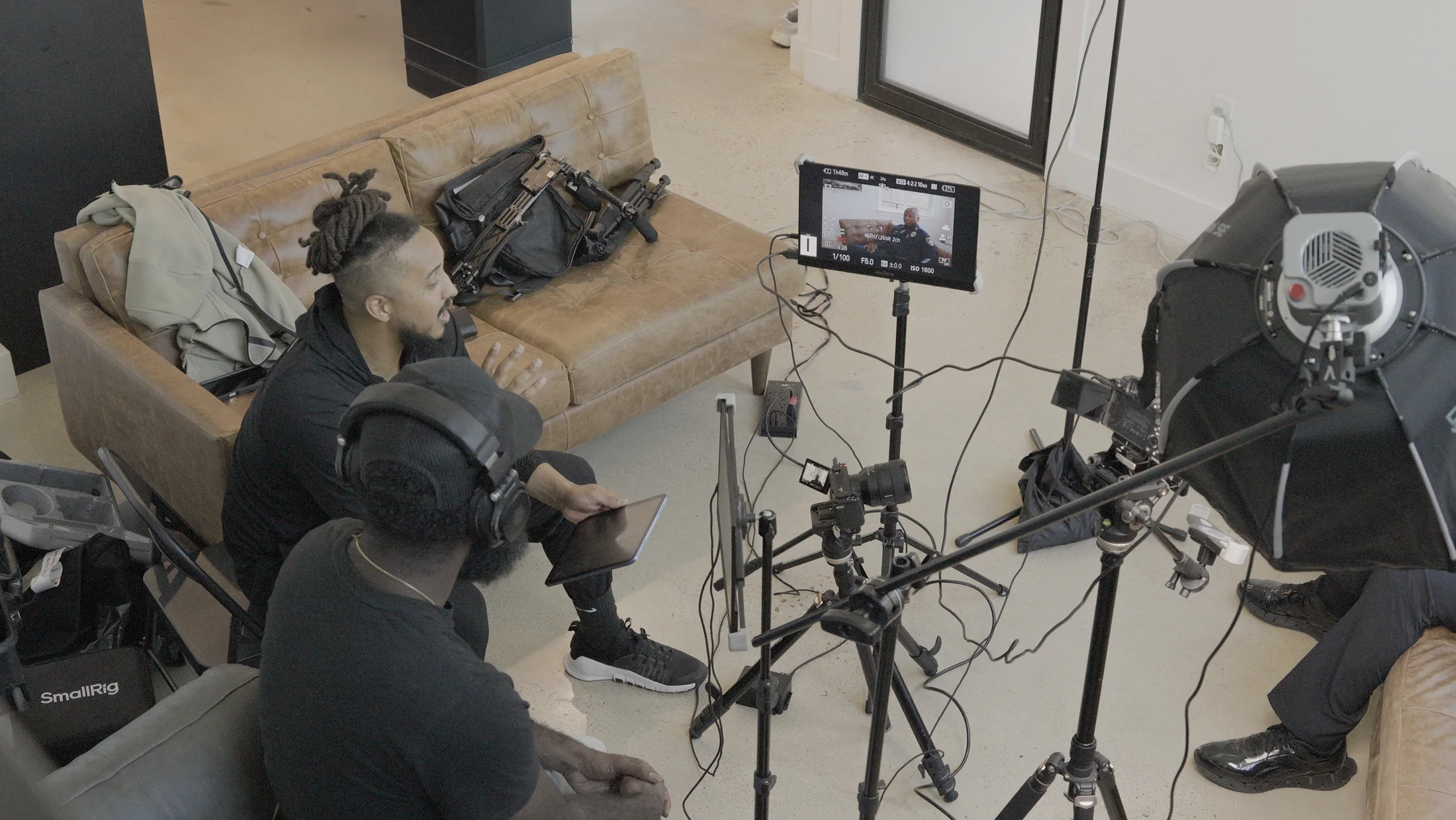 Ronnie Lillard directs an interview on set beside a sound operator, with a police officer on the camera monitor