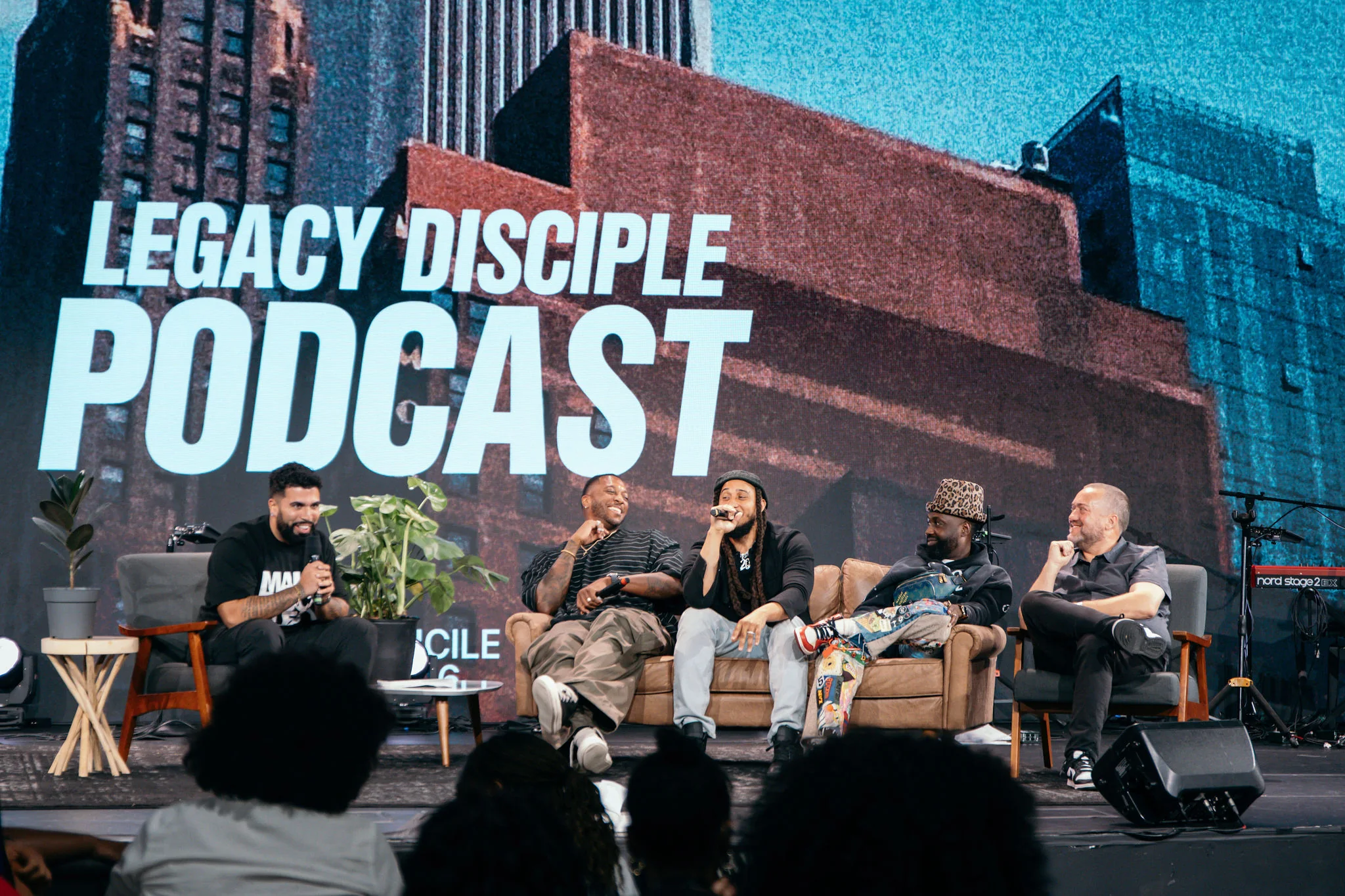 Ronnie Lillard speaks into a microphone on a stage panel with four other men
